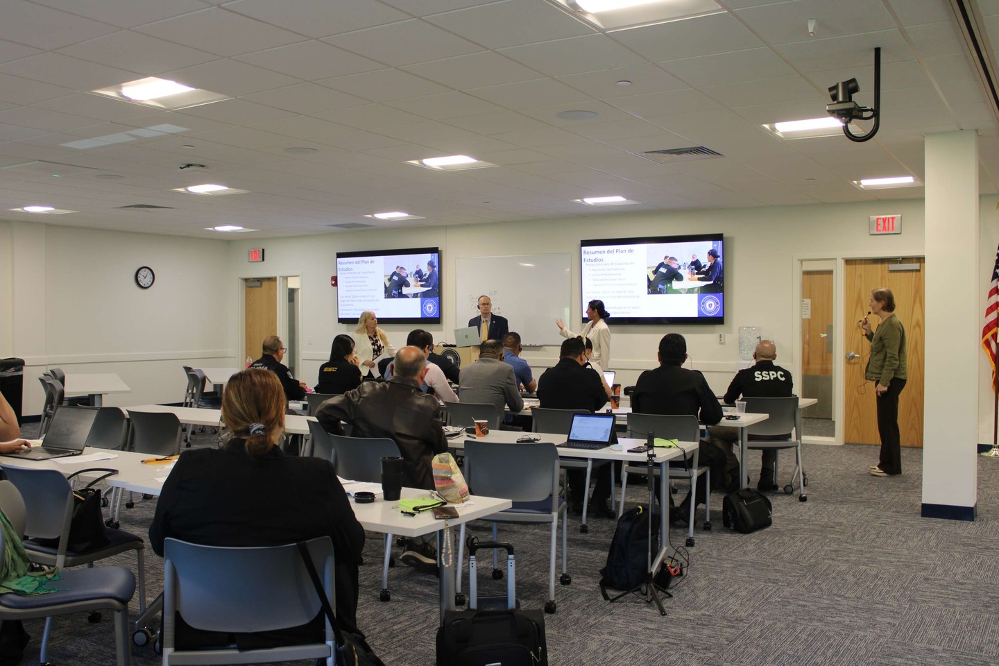 Instructor-led training session in a classroom with dual wall displays and a ceiling-mounted PTZ camera
