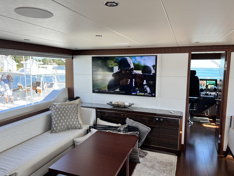 Finished yacht salon with a large frameless wall-mounted TV playing ESPN above the seating area, marina views through the windows and the galley beyond.