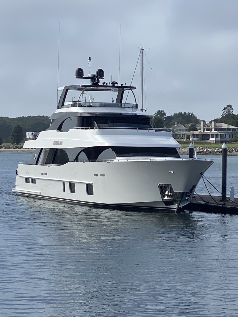 The motor yacht at anchor on calm water, twin KVH satellite domes visible atop the hardtop mast.