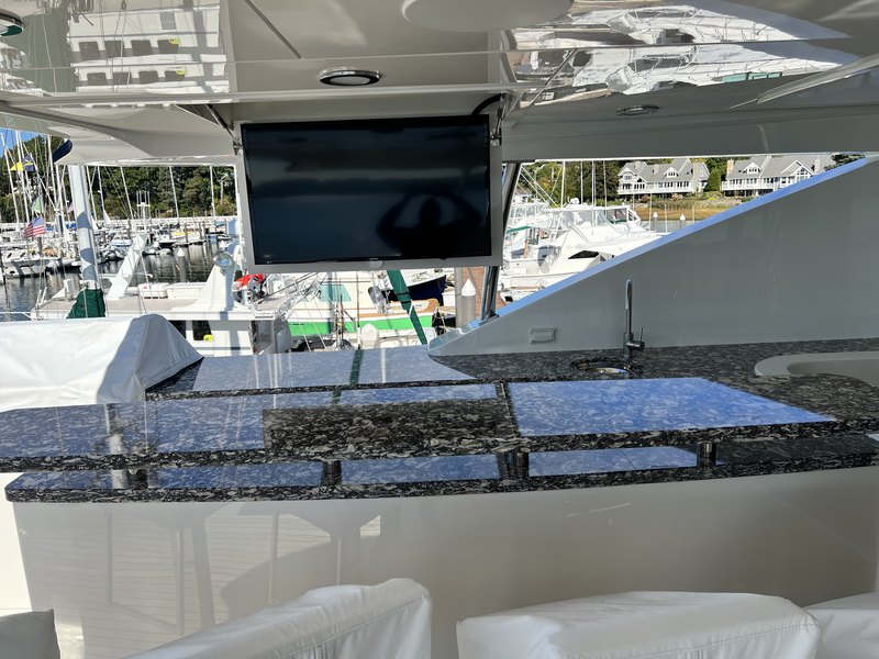 A pop-up TV lift raised from the flybridge wet bar's marbled stone countertop, with the marina and waterfront homes in the background.