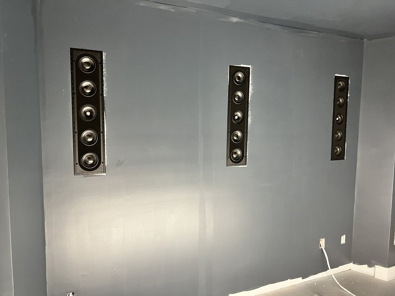 Clean angled view of three flush-mounted in-wall Sonance LCR speaker arrays in the dark slate theater front wall.