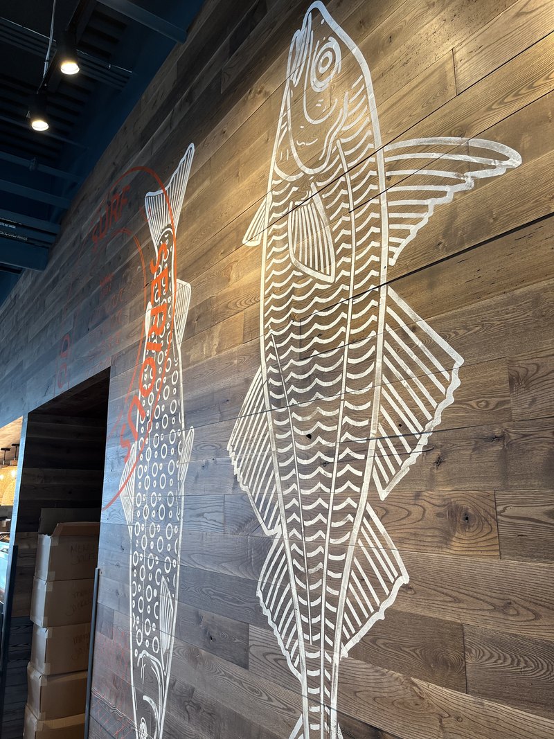 Striking wood-plank ceiling with large white stenciled fish murals and orange 'Serious' branding, with small architectural accent lights visible along the soffit.