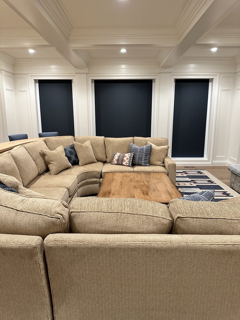 Great room with the motorized blackout roller shades fully lowered, turning the triple window wall completely dark and showing the room-darkening capability alongside recessed ceiling lighting; image is stored rotated 90 degrees sideways and needs rotation before use.